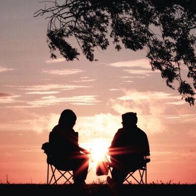 Two people sit together under a tree while the sun goes down.