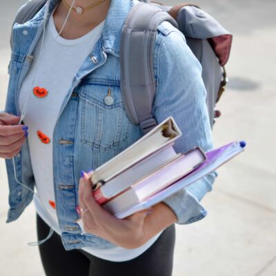 A student wearing a denim jacket carries books as she works toward her behavioral health workforce degree.